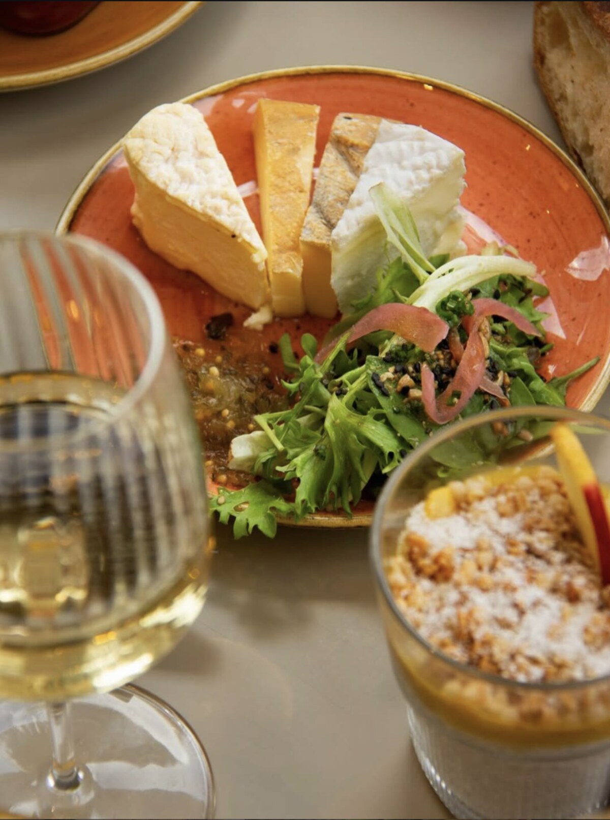 Plateau de fromages locaux et salade verte, servis avec un verre de vin